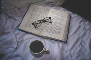 **Optimized Alt Text for SEO:**"Open book on white bed with black-framed glasses and ceramic mug of coffee; ideal setup for podcast note-taking or watching CreatorPoint YouTube videos"**SEO Best Practices Used:**
1. **Keyword Optimization:** Including relevant keywords such as "book," "white bed," "black-framed glasses," "ceramic mug of coffee," and specific use cases like "podcast note-taking" and "CreatorPoint YouTube videos."
2. **Descriptive Phrasing:** Ensuring the description is rich without being excessively wordy.
3. **Contextual Relevance:** Mentioning specific activities (podcast note-taking, watching YouTube) to capture targeted searches.This alt text maintains the essential details while aligning with relevant keywords that can boost indexing performance on Google. Creatorpoint – Creator Knowledge, Simplified. The best resources, podcast summaries, and learning for creators.