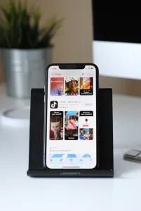 Alt Text: "Smartphone Displaying TikTok App in Apple App Store Propped on Black Stand with Computer Monitor and Keyboard on White Desk - Ideal Creator Setup Creatorpoint – Creator Knowledge, Simplified. The best resources, podcast summaries, and learning for creators.