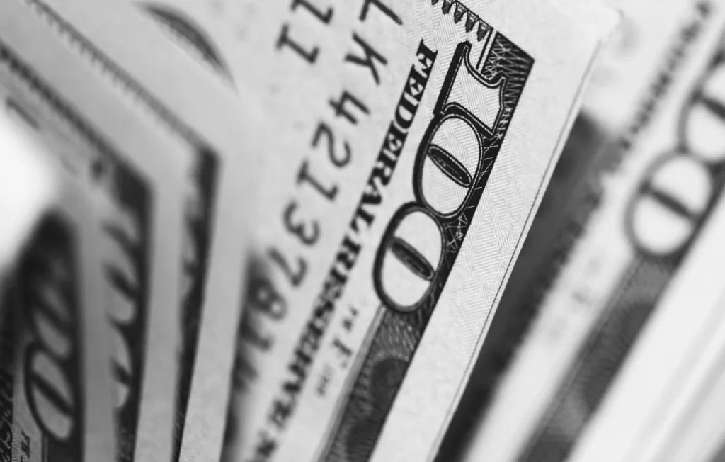 Close-up of several hundred-dollar bills fanned out, symbolizing financial rewards of learning how to make money writing. Central bill shows the number 100 prominently, conveying wealth potential. Grayscale image emphasizes details and focus on prosperity through writing as a career. Creatorpoint – Creator Knowledge, Simplified. The best resources, podcast summaries, and learning for creators.
