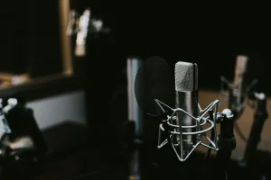 Alt text: "Professional condenser microphone with pop filter in dimly lit recording studio, featuring blurred background with another mic and soundproofing equipment—ideal for podcast or YouTube content creation. Creatorpoint – Creator Knowledge, Simplified. The best resources, podcast summaries, and learning for creators.