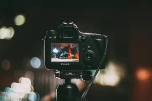 Alt text: "Canon DSLR camera on tripod capturing vibrant night scene with buildings and neon lights, showcased on LCD screen. Blurred bokeh background emphasizes camera focus. Ideal for YouTube creators and photography enthusiasts seeking stunning visuals. Creatorpoint – Creator Knowledge, Simplified. The best resources, podcast summaries, and learning for creators.
