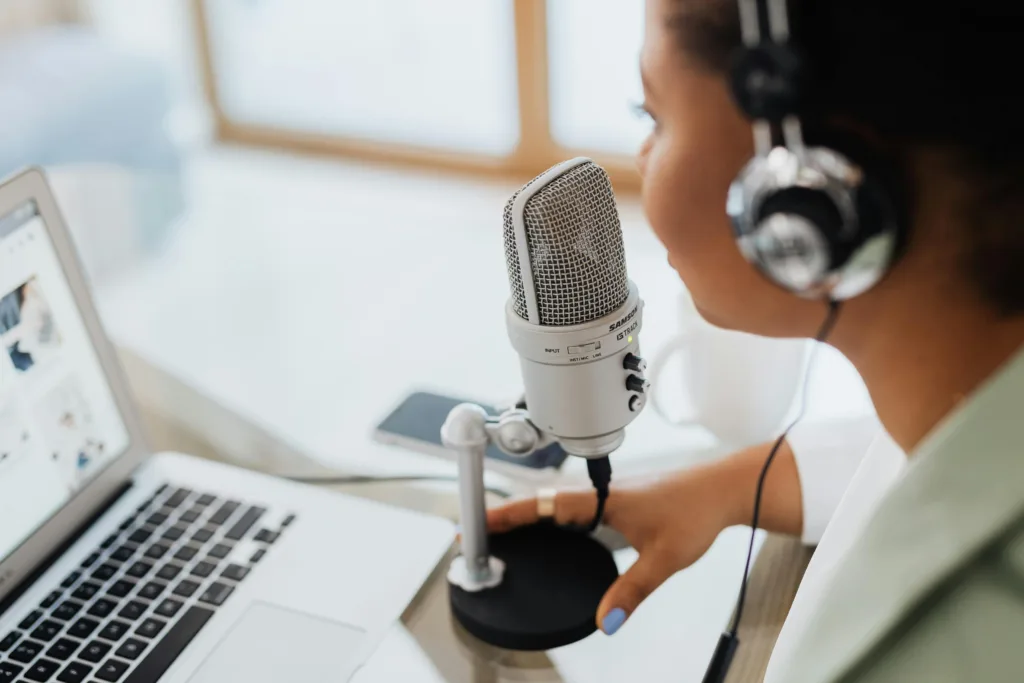 Person wearing headphones speaking into a microphone on a stand at a desk with an open laptop, discussing "how to start a YouTube channel," holding the microphone base. Creatorpoint – Creator Knowledge, Simplified. The best resources, podcast summaries, and learning for creators.