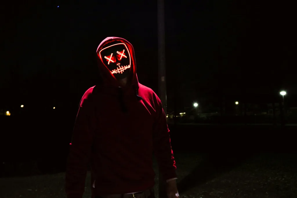 Alt text: "Individual in red hoodie and illuminated mask with stitched eyes and mouth, standing in dimly lit eerie setting for podcast summary or creator point discussion. Creatorpoint – Creator Knowledge, Simplified. The best resources, podcast summaries, and learning for creators.