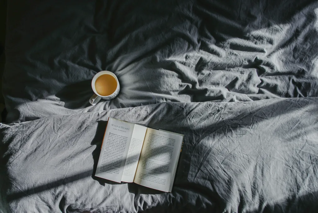 Cozy morning relaxation – mug of coffee beside an open book on grey bedspread, sunlight casting warm shadows – perfect post-podcast reading. Creatorpoint – Creator Knowledge, Simplified. The best resources, podcast summaries, and learning for creators.