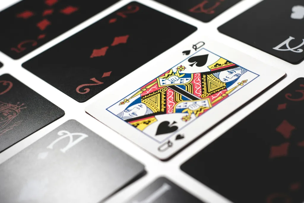 Close-up of playing cards on a white surface featuring the Queen of Spades at the center, surrounded by various red diamonds and black spades suits. Perfect metaphor for faceless YouTube channel ideas in terms of intrigue and mystery. Creatorpoint – Creator Knowledge, Simplified. The best resources, podcast summaries, and learning for creators.