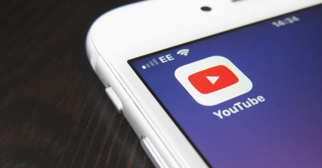 Close-up of a smartphone showing the YouTube app icon, guiding on how to start a YouTube channel. Partially visible white phone edge on dark surface. Status bar highlights mobile signal and battery life. Perfect for beginners looking to create a successful YouTube presence. Creatorpoint – Creator Knowledge, Simplified. The best resources, podcast summaries, and learning for creators.