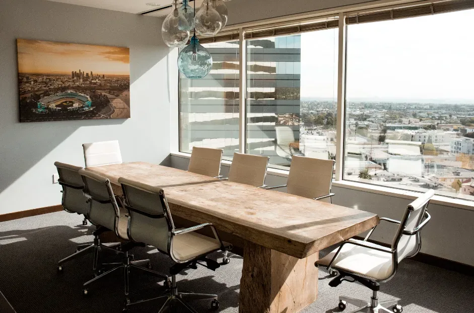 Modern conference room with a wooden table and eight white chairs for YouTube channel brainstorming. Large windows provide cityscape views, enhancing inspiration. Cityscape painting decorates the wall, while pendant lights foster creativity. Perfect space for innovative ideas and content creation. Creatorpoint – Creator Knowledge, Simplified. The best resources, podcast summaries, and learning for creators.