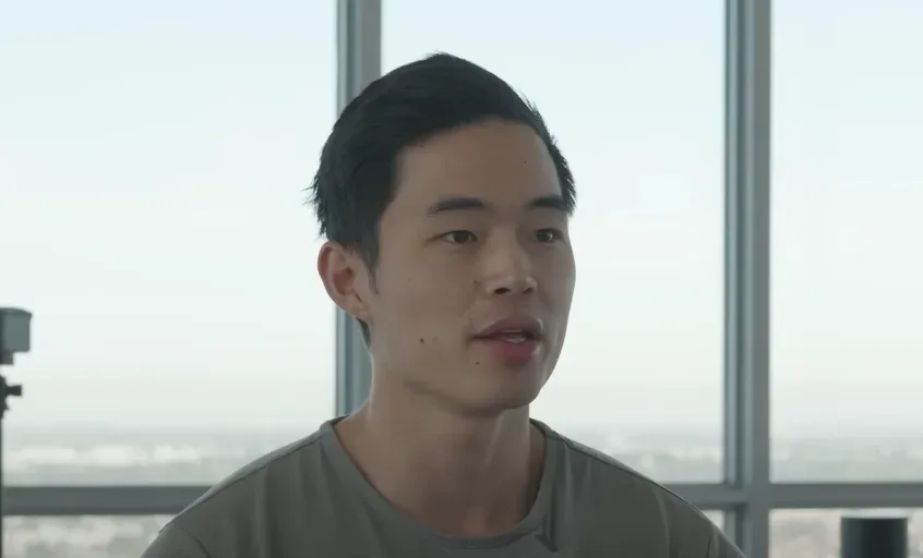 A person with short black hair sits by a large window, wearing a gray T-shirt, contemplating how to start a YouTube channel. The cityscape in the background symbolizes endless opportunities and potential for success on YouTube. Ideal for aspiring creators seeking inspiration and motivation. Creatorpoint – Creator Knowledge, Simplified. The best resources, podcast summaries, and learning for creators.