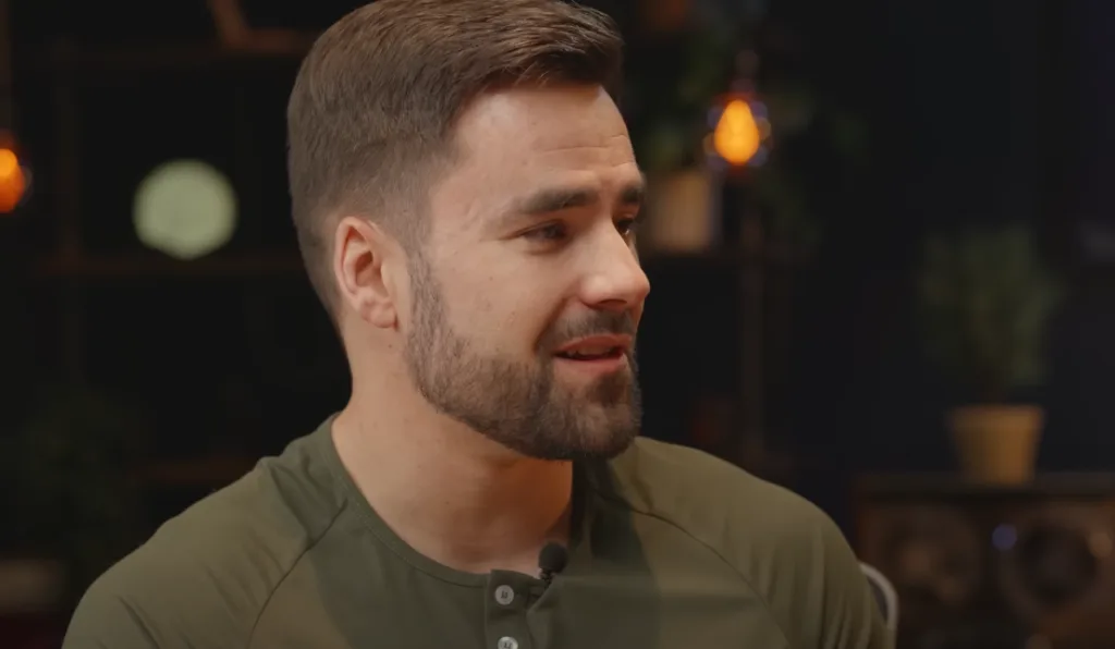 Man with short brown hair and beard wearing a green henley shirt gazes thoughtfully to the side, pondering how to market Notion templates. Neutral expression against a blurred background of lights and greenery, conveying creativity and focus in digital product promotion strategy. Creatorpoint – Creator Knowledge, Simplified. The best resources, podcast summaries, and learning for creators.