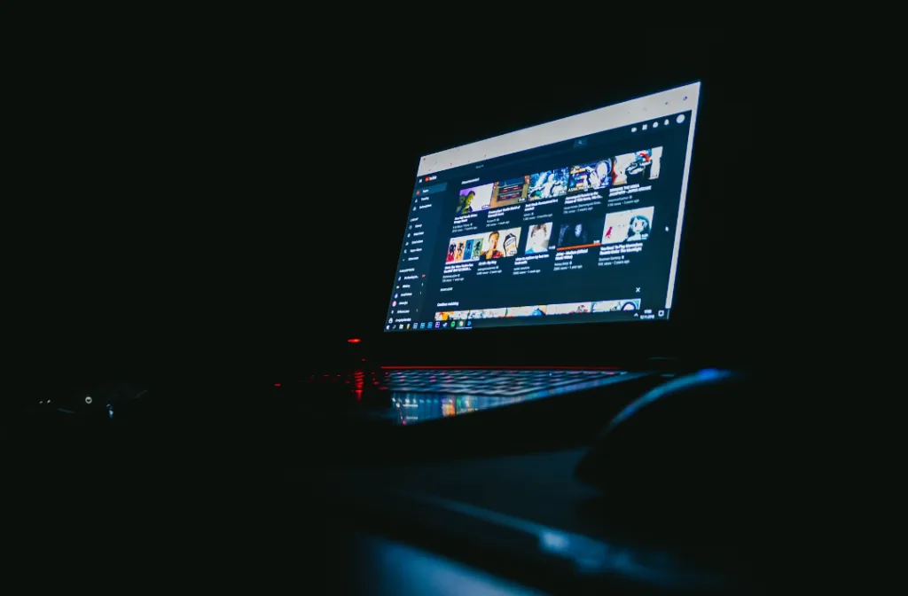 Laptop in a dark room with an illuminated screen displaying YouTube videos and thumbnails, emphasizing YouTube tips and tricks. Mouse visible next to the laptop. #YouTubeTips #VideoTutorials #SEO# Creatorpoint – Creator Knowledge, Simplified. The best resources, podcast summaries, and learning for creators.