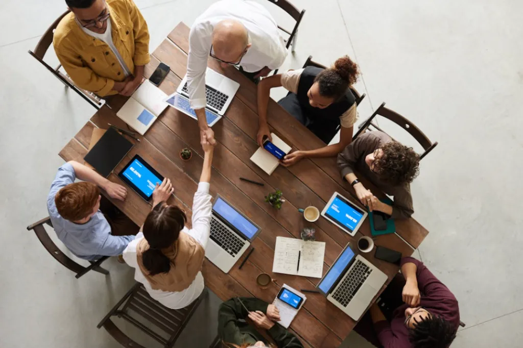 Business meeting with diverse group around wooden table, laptops and smartphones visible. Two central individuals shaking hands, inspiring solo business ideas. Collaborative workspace setting indicating professional networking and brainstorming session for innovative entrepreneurship growth. Creatorpoint – Creator Knowledge, Simplified. The best resources, podcast summaries, and learning for creators.