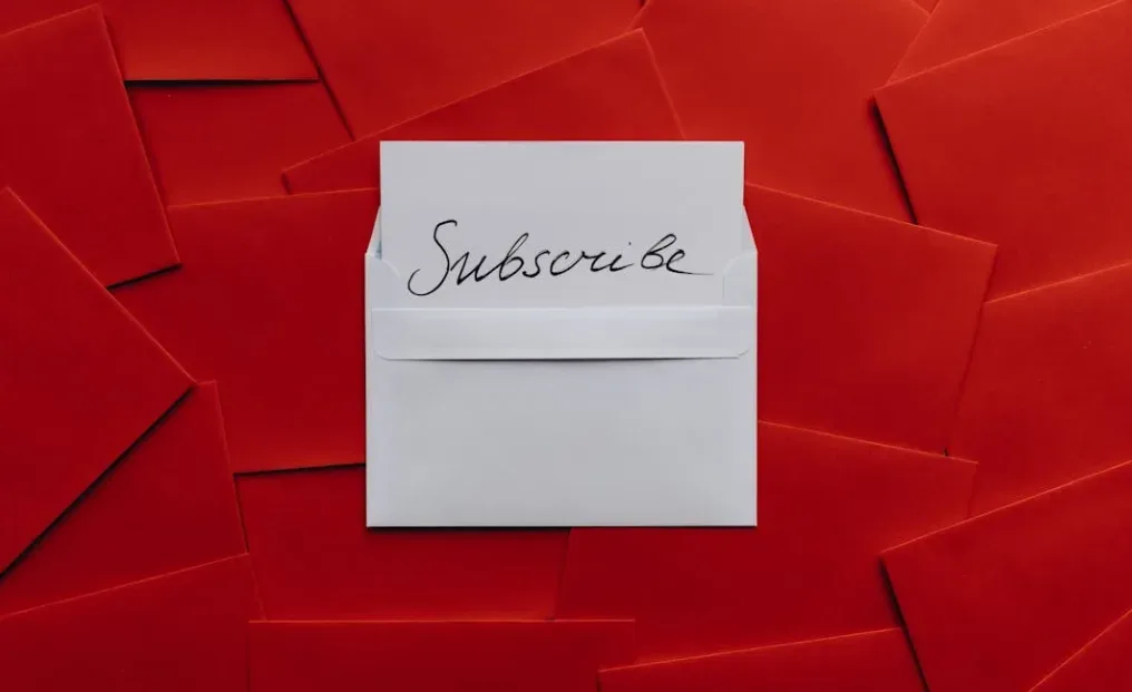 White envelope with "Subscribe" in cursive on top of red envelopes background, symbolizing digital product ideas and excitement, viewed from above. Creatorpoint – Creator Knowledge, Simplified. The best resources, podcast summaries, and learning for creators.