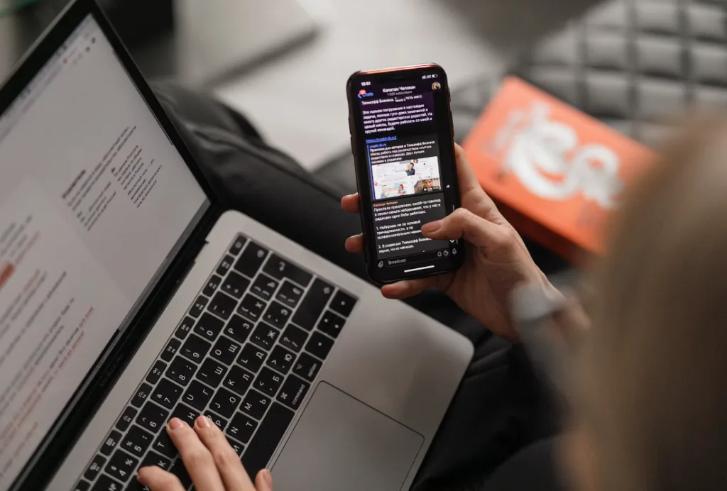 Person using smartphone messaging app and brainstorming digital product ideas on laptop, focusing on creativity. Text displayed on screen emphasizes innovation. Partially visible orange book adds color to the scene, creating a dynamic and inspiring workspace. Creatorpoint – Creator Knowledge, Simplified. The best resources, podcast summaries, and learning for creators.