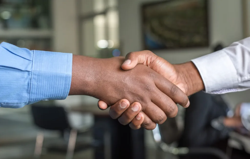 Professional office handshake between two individuals, one in a blue shirt and the other in white, symbolizing collaboration and strategic connections. Crisp details emphasize the meeting, akin to exploring unique faceless YouTube channel ideas. Blurred background ensures attention on dynamic interaction. Creatorpoint – Creator Knowledge, Simplified. The best resources, podcast summaries, and learning for creators.