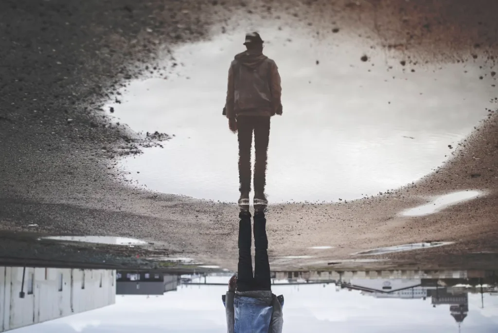Person standing on a wet gravel surface with their reflection in a large puddle. Industrial scenery inspires faceless YouTube channels, with distant buildings sparking endless creative ideas. Perfect urban landscape for content creators seeking fresh, innovative perspectives and inspiration. Creatorpoint – Creator Knowledge, Simplified. The best resources, podcast summaries, and learning for creators.
