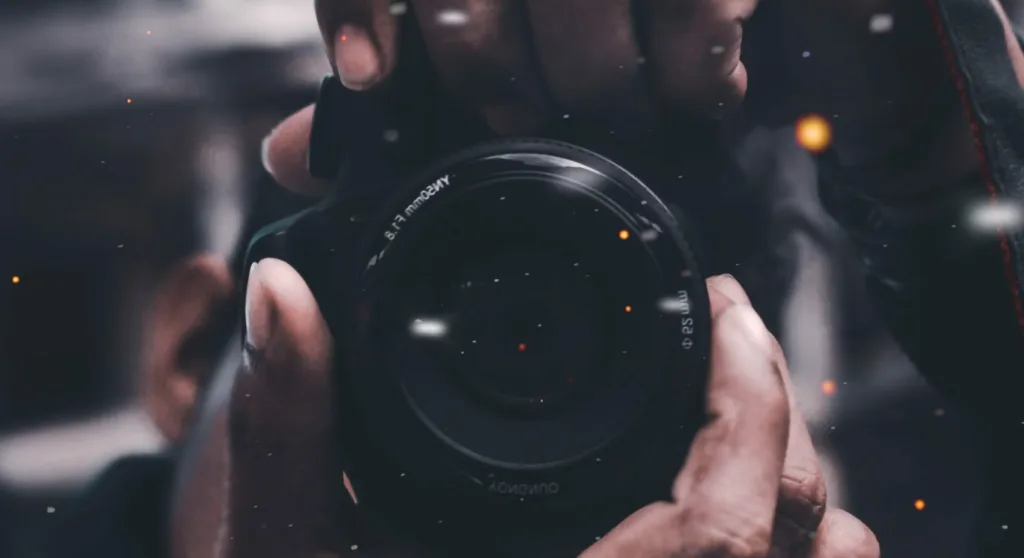 Close-up of hands gripping a camera lens, emphasizing focus and creativity. Blurred background with glowing particles illustrates how compelling visuals attract YouTube Shorts views. Perfect for visual storytelling and mastering viewer engagement on video platforms. Creatorpoint – Creator Knowledge, Simplified. The best resources, podcast summaries, and learning for creators.