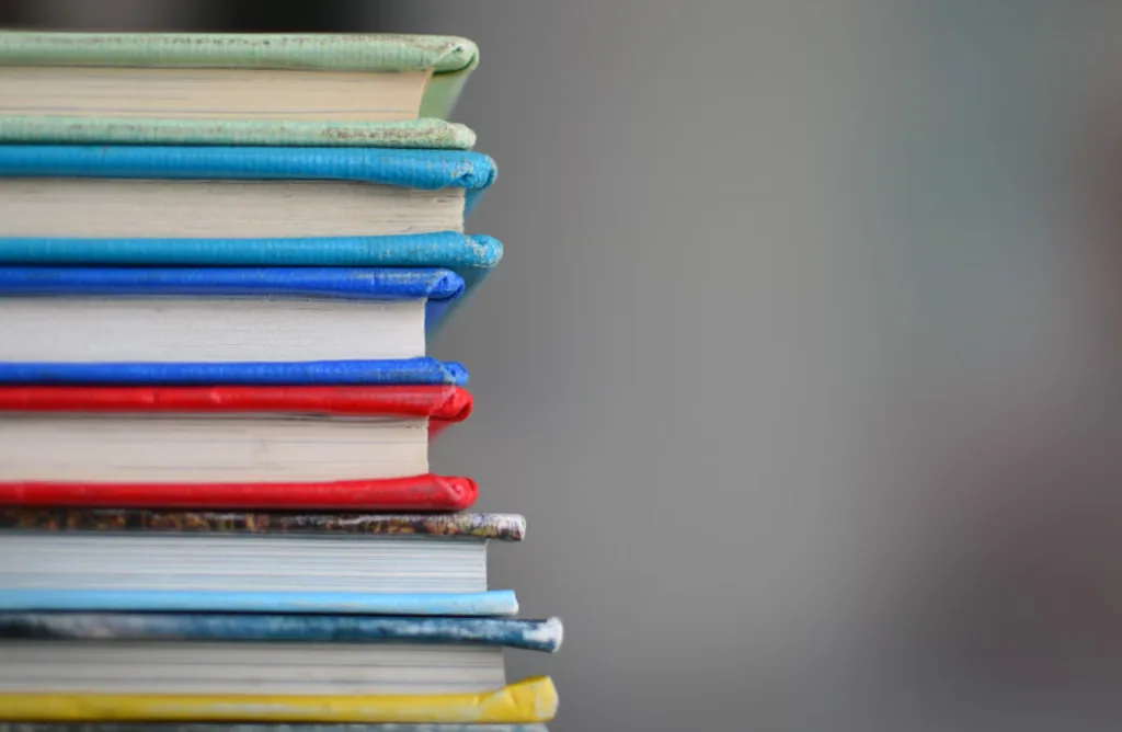 Vibrant stack of hardcover books with colorful spines—blue, green, red, yellow—set against a blurred gray background. Eye-catching like dynamic thumbnails grabbing attention on YouTube Shorts. Perfect for readers seeking engaging content and visually appealing book arrangements. Creatorpoint – Creator Knowledge, Simplified. The best resources, podcast summaries, and learning for creators.