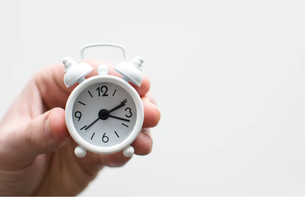 Hand holding a white analog alarm clock at 10:10 against plain background, symbolizing perfect timing like optimal YouTube Shorts posting times. Minimalistic black hands represent precision and simplicity in content creation, enhancing your chances of first-page Google indexing for SEO success. Creatorpoint – Creator Knowledge, Simplified. The best resources, podcast summaries, and learning for creators.